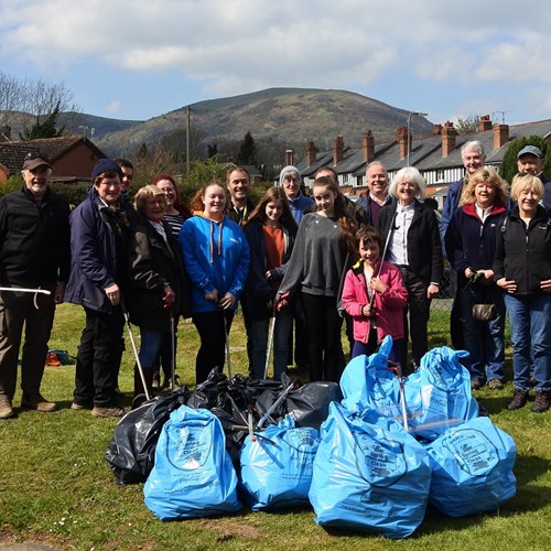 A group of people stand behind a large pile of big bags full of litter they've collected